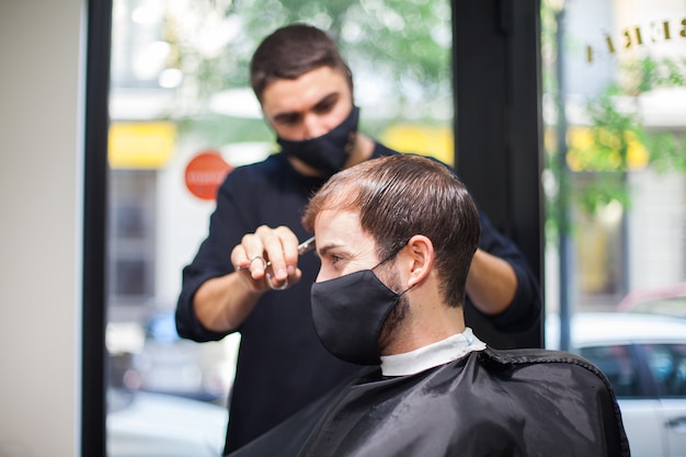 Ein professioneller Friseur mit Schutzmaske schneidet einem Kunden während des Coronavirus die Haare