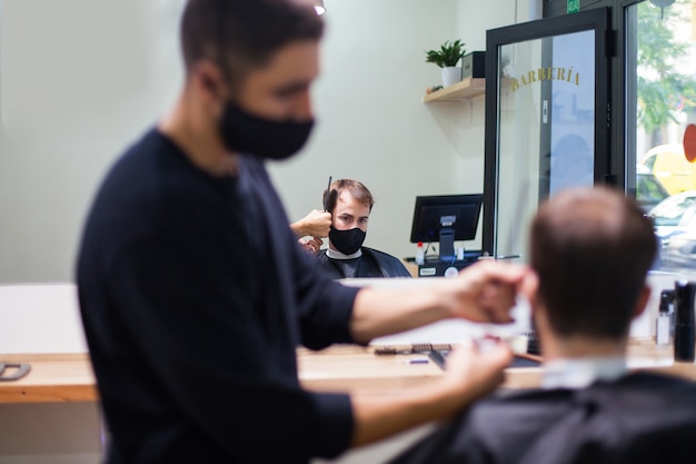 Ein professioneller Friseur mit Schutzmaske schneidet einem Kunden während des Coronavirus die Haare