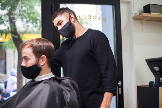 Ein professioneller Friseur mit Schutzmaske schneidet einem Kunden während des Coronavirus die Haare