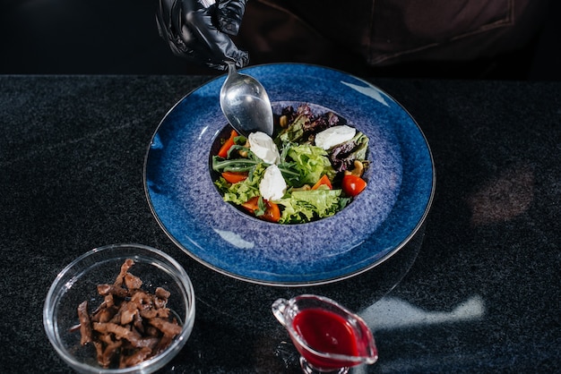 Ein professioneller Koch bereitet in einem modernen und stilvollen Restaurant einen köstlichen frischen Salat aus grünem Gemüse und saftigem Kalb zu