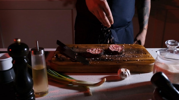 Ein professioneller Koch streut ein Stück gekochtes Fleisch mit grobem Salz. Das Konzept des Kochens von köstlichem Essen