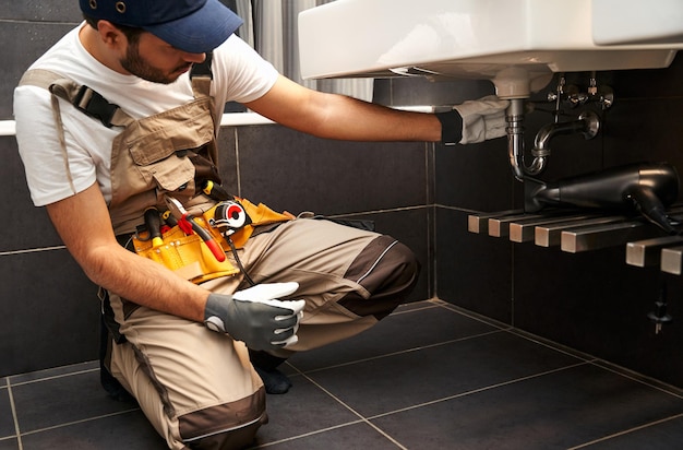 Ein professioneller Mann in Uniform repariert zu Hause ein Badezimmerbecken