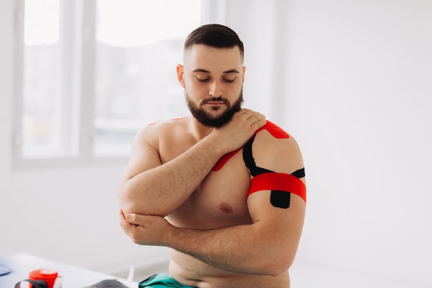 Ein professioneller Physiotherapeut, der ein dehnbares Kinesiologieband auf Arm und Schulter des Patienten klebt.