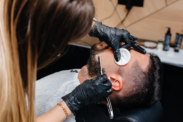 Ein professioneller Stylist in einem modernen, stilvollen Friseursalon rasiert und schneidet einem jungen Mann die Haare. Schönheitssalon, Friseursalon.