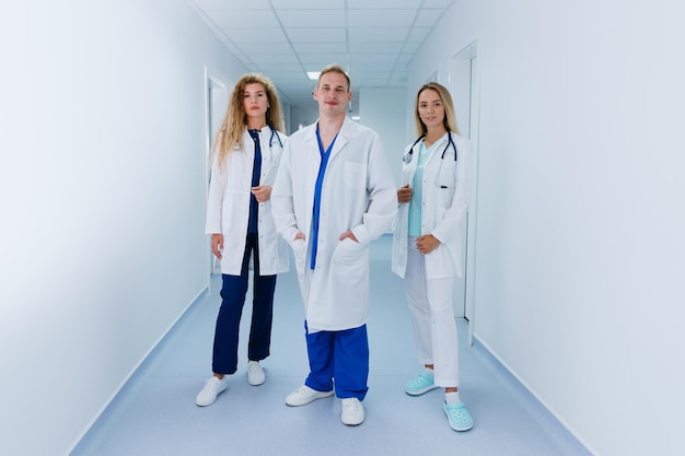 Ein professionelles Ärzteteam steht auf dem Flur des Krankenhauses. Kollegen in OP-Anzügen und weißen Kitteln schauen in die Kamera