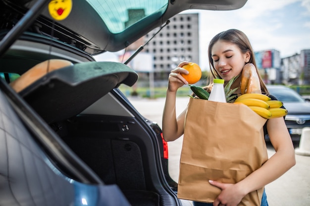 Ein Prozess der jungen Frau, die Lebensmittel aus einem Supermarkt vom Trolley zum Auto-LKW nimmt