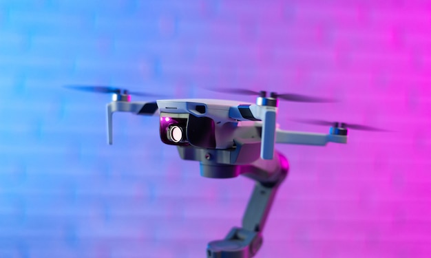 Ein Quadrocopter mit einer Drohnenkamera. Ein kleiner unbemannter Quadcopter steht auf einem Stabilisatorständer für ein Telefon gegen eine schöne Neon-Ziegelwand