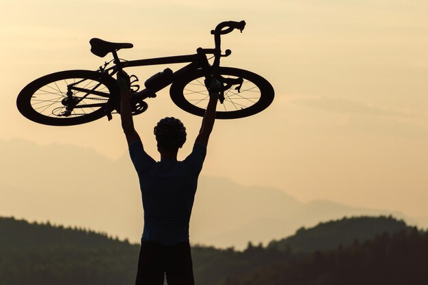 Ein Radfahrer erhebt sich mit einem Fahrrad über seinem Kopf und schaut auf den Sonnenuntergang