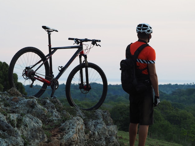 Ein Radfahrer steht auf einem Hügel, mit dem Mountainbike in der Abenddämmerung. Am Horizont der Atlantik. Aktiver Lebensstil.