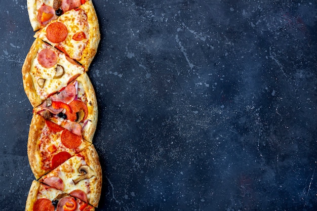 Ein Rahmen von Scheiben Peperoni-Pizza mit Salami, Pilzen, Schinken und Käse auf einem dunklen Hintergrund. Italienisches traditionelles Mittag- oder Abendessen. Fast Food und Street Food Konzept. Flach liegen