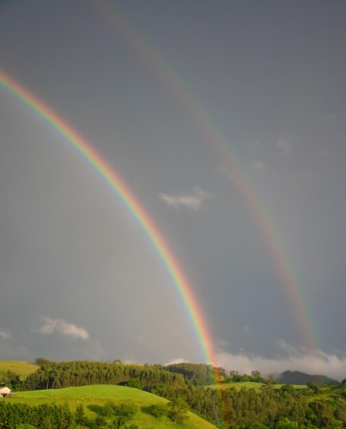 Ein Regenbogen und seine Reflexion in einer Landschaft aus grünen Wiesen in Kantabrien (Spanien)