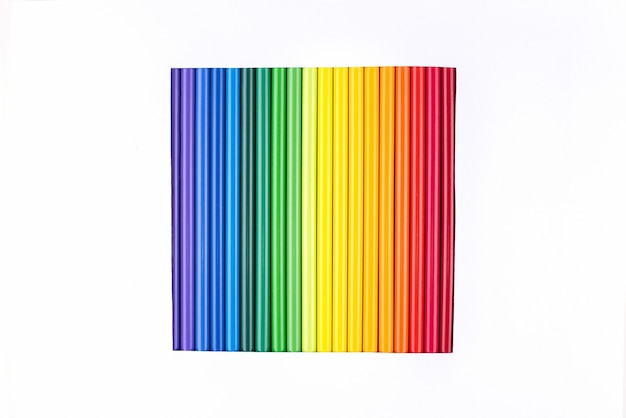 Ein Regenbogen von Stiften in einem ausgeschnittenen Quadrat auf einem weißen Papierhintergrund.