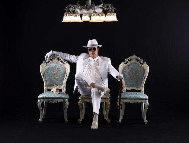 Foto ein reicher herr in einem weißen anzug sitzt auf einem stuhl mit schwarzem studiohintergrund