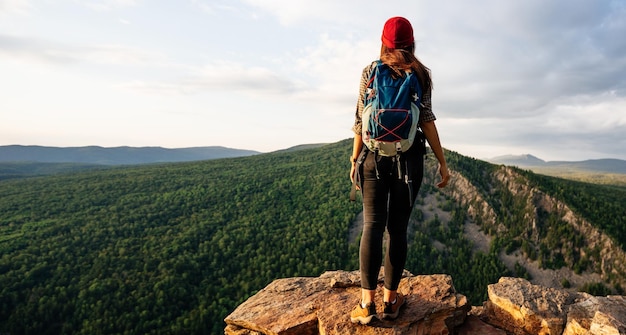 Ein Reisender auf dem Hintergrund der Berge bei Sonnenuntergang, Panoramablick. Eine junge Touristenfrau mit Rucksack genießt den Sonnenuntergang vom Gipfel des Berges. Ein Reisender auf dem Hintergrund der Berge.