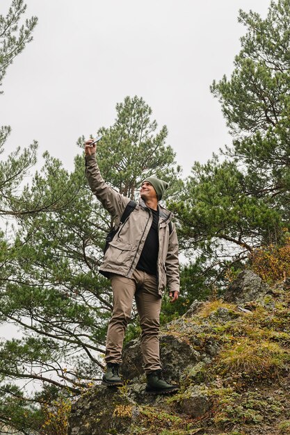 Ein Reisender mit Rucksack steht am Rand des Berges und macht ein Selfie-Foto auf seinem Handy