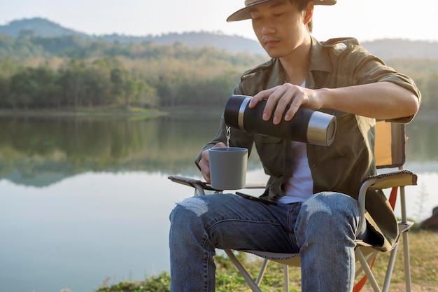 Ein Reisender trinkt heißen Kaffee über dem Konzept des Camping-Naturtourismus mit Berg- und Flussblick