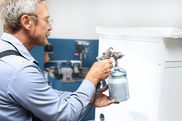 Ein Rentner mit grauen Haaren und Brille lackiert Metallprodukte Zusatzverdienst für eine ältere Person