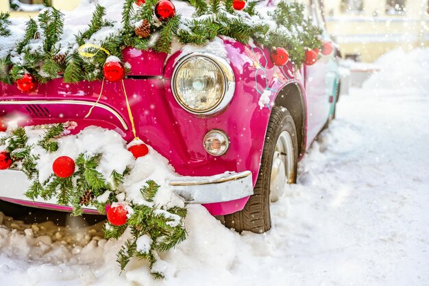 Ein Retro-Auto, das mit Weihnachtsspielzeug aus Fichtenzweigen dekoriert und mit Schnee bedeckt ist