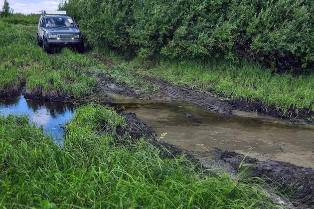 Ein riesiger blauer SUV fährt im Gelände und die Straße führt direkt in den Sumpf