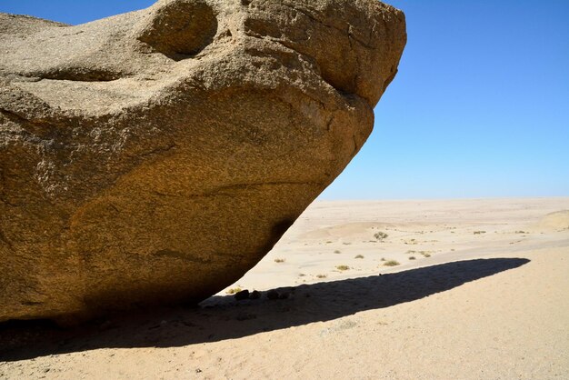 Ein riesiger Felsblock mit einem Schatten liegt in der Wüste unter einem blauen Himmel