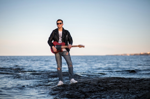 Ein Rockgitarrist mit Gitarre in der Hand in Sonnenbrille und Bikerjacke steht