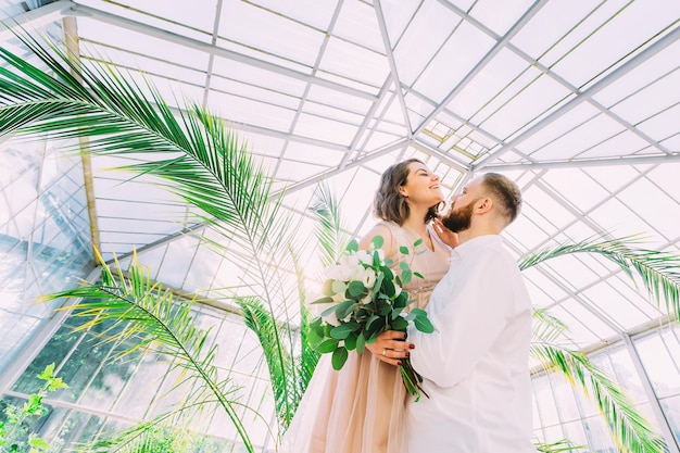 Ein romantisches frisch verheiratetes Paar Braut und Bräutigam steht und hält einen Blumenstrauß im botanischen Garten Hochzeitszeremonie in der Natur