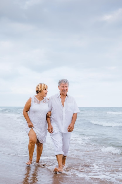 Ein romantisches Seniorenpaar geht am Strand gegen den Himmel spazieren
