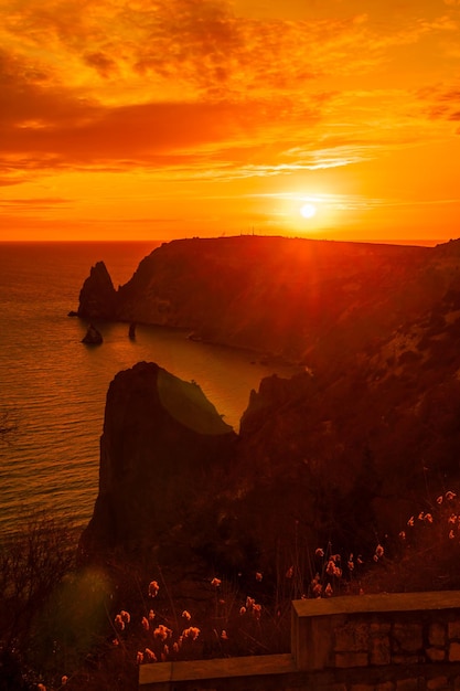 Ein rot brennender Sonnenuntergang mit der Silhouette einer Klippe über dem Meer