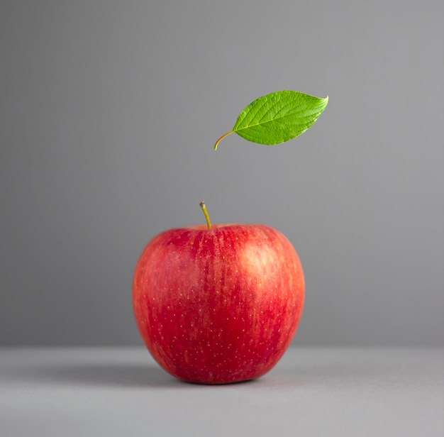 Ein roter Apfel mit grünem Blatt auf grauem Hintergrund