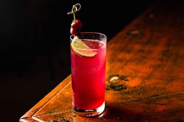 Ein roter Cocktail in einem mit Zitrone und Kirschen garnierten Highballglas