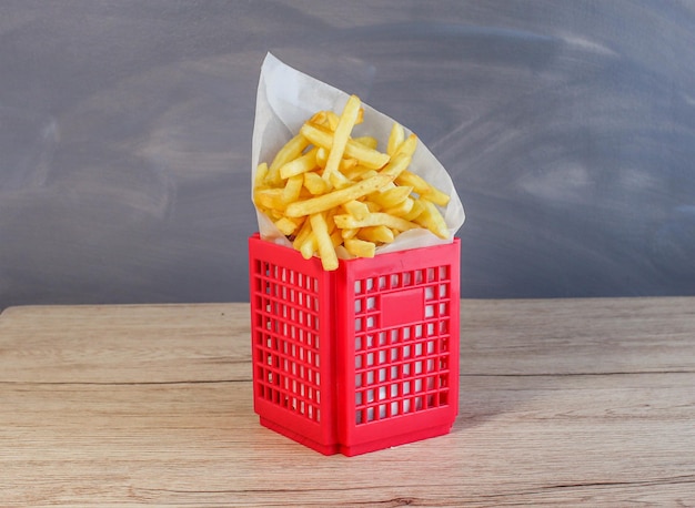 Ein roter Korb mit Französisch auf einem Holztisch Ein Korb mit Pommes frites auf einem Holztisch