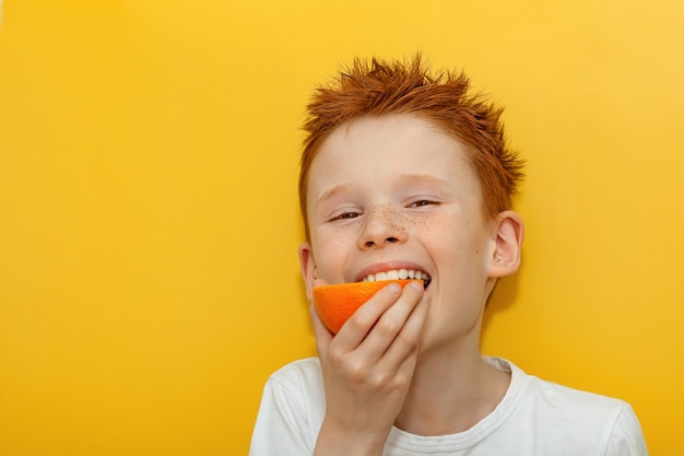 Ein rothaariger Junge beißt appetitlich in eine saftige Orange auf gelbem Grund