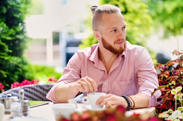 Ein rothaariger Mann in einem rosafarbenen Hemd trinkt Kaffee in einem Open-Air-Café.