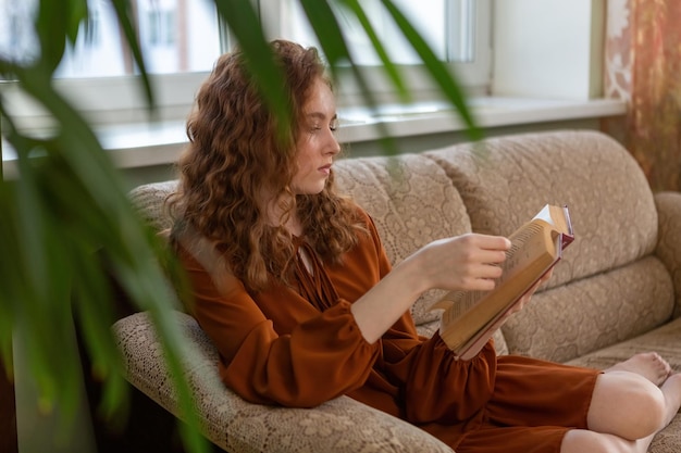 Ein rothaariges Mädchen liest zu Hause auf der Couch ein Buch