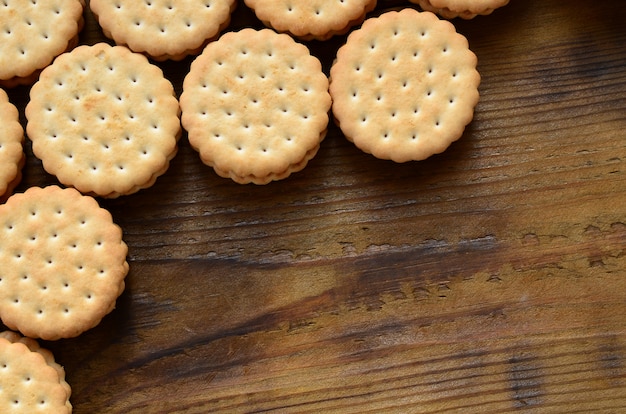 Ein runder Sandwichkeks mit Kokosnussfüllung liegt in großen Mengen auf einer braunen Holzoberfläche