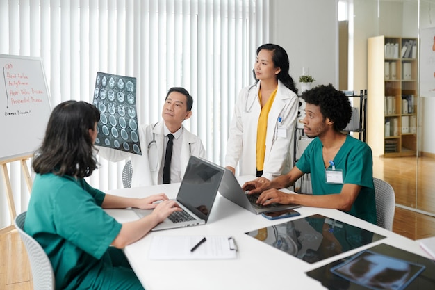 Ein Ärzteteam betrachtet das Röntgenbild der Bandscheiben, während Krankenschwestern am Laptop tippen