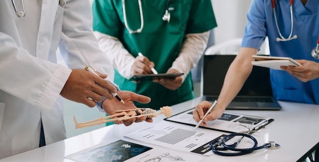 Ein Ärzteteam trifft sich mit Ärzten in weißen Laborkitteln und OP-Kitteln, die an einem Schreibtisch sitzen und über einen Patienten sprechen, der online mit Computern in der medizinischen Industrie arbeitetxA