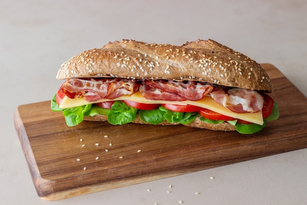 Ein Sandwich aus dunklem Brot mit Salat, Speck, Tomaten und Käse. Frühstück. Fast Food.