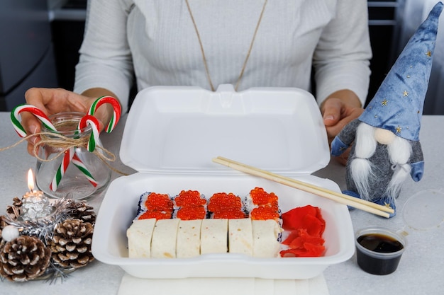 Ein Satz asiatischer Brötchen in einer Plastikbox zu Hause in der Küche in festlichem Stil Das Mädchen hält Essen mit Stäbchen Weihnachtskonzept Dekorationen für das neue Jahr