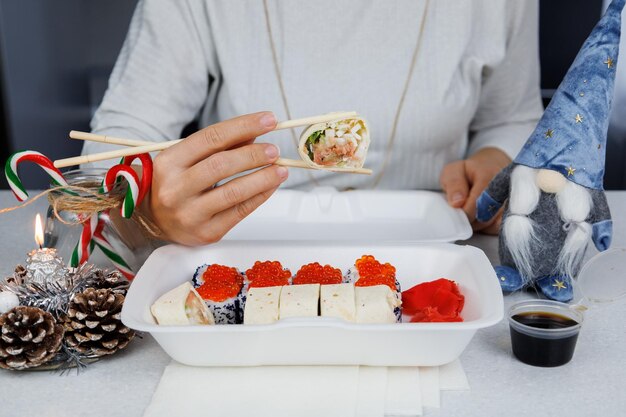 Foto ein satz asiatischer brötchen in einer plastikbox zu hause in der küche in festlichem stil das mädchen hält essen mit stäbchen weihnachtskonzept dekorationen für das neue jahr