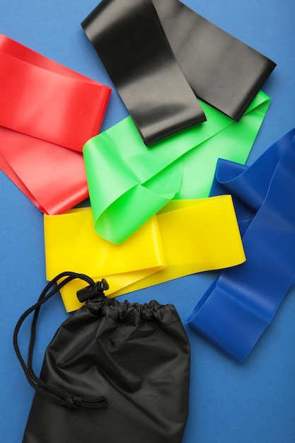 Ein Satz bunter Latex-Gummibänder für Fitness und eine schwarze Hülle dafür auf blauem Hintergrund. Vertikales Foto des Sportkonzepts