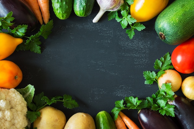 Ein Satz Frischgemüse (Gurken, Tomaten, Kohl, Karotten, Knoblauch, Zwiebeln), vereinbart in einem Kreis auf einem schwarzen Hintergrund