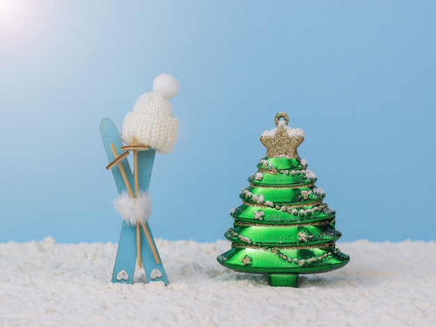 Ein Satz Ski mit Stöcken, einer Strickmütze und einem verzierten Tannenbaum im Schnee auf blauem Hintergrund. Das Konzept der Weihnachtsferien und des Wintersports.