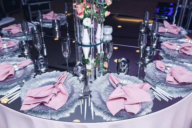 Ein schicker Spiegeltisch, der in einem Restaurant serviert wird Pinke Servietten auf silbernen Tellern