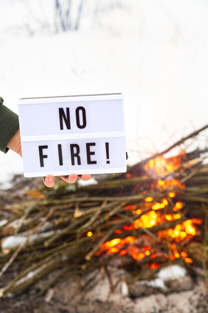 Foto ein schild mit dem text  ⁇ kein feuer in der hand eines mannes ⁇  über einem flammenden lagerfeuer auf weißem hintergrund