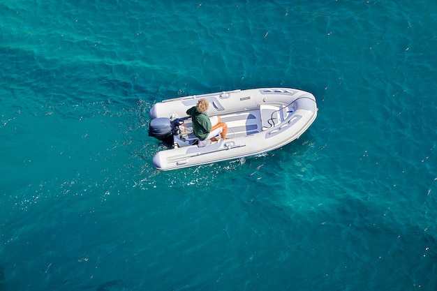 Ein Schlauchboot schwimmt langsam mit einem Motor auf dem azurblauen Meer. Bootsfahrt an einem sonnigen Sommertag.