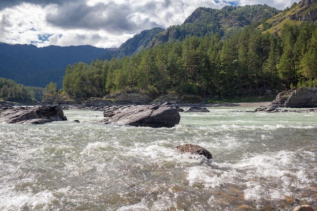 Ein schnell fließender breiter und voll fließender Gebirgsfluss. Große Felsen ragen aus dem Wasser.