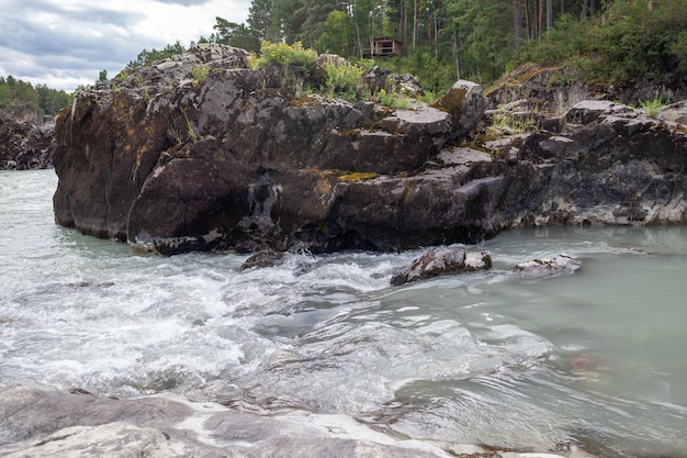 Ein schnell fließender breiter und voll fließender Gebirgsfluss. Große Felsen ragen aus dem Wasser.