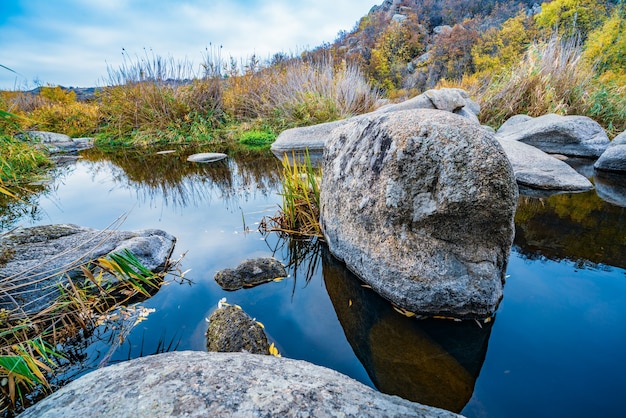 Ein schneller, flacher, sauberer Bach fließt zwischen glatten, nassen großen Steinen, umgeben von hohen trockenen Klumpen, die sich in der malerischen Ukraine im Wind wiegen