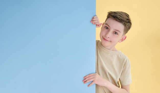 Ein schöner Junge hält ein blaues Blatt Papier, ein weißes Schild auf weißem Hintergrund zeigt die Klasse mit seiner Hand und lächelt